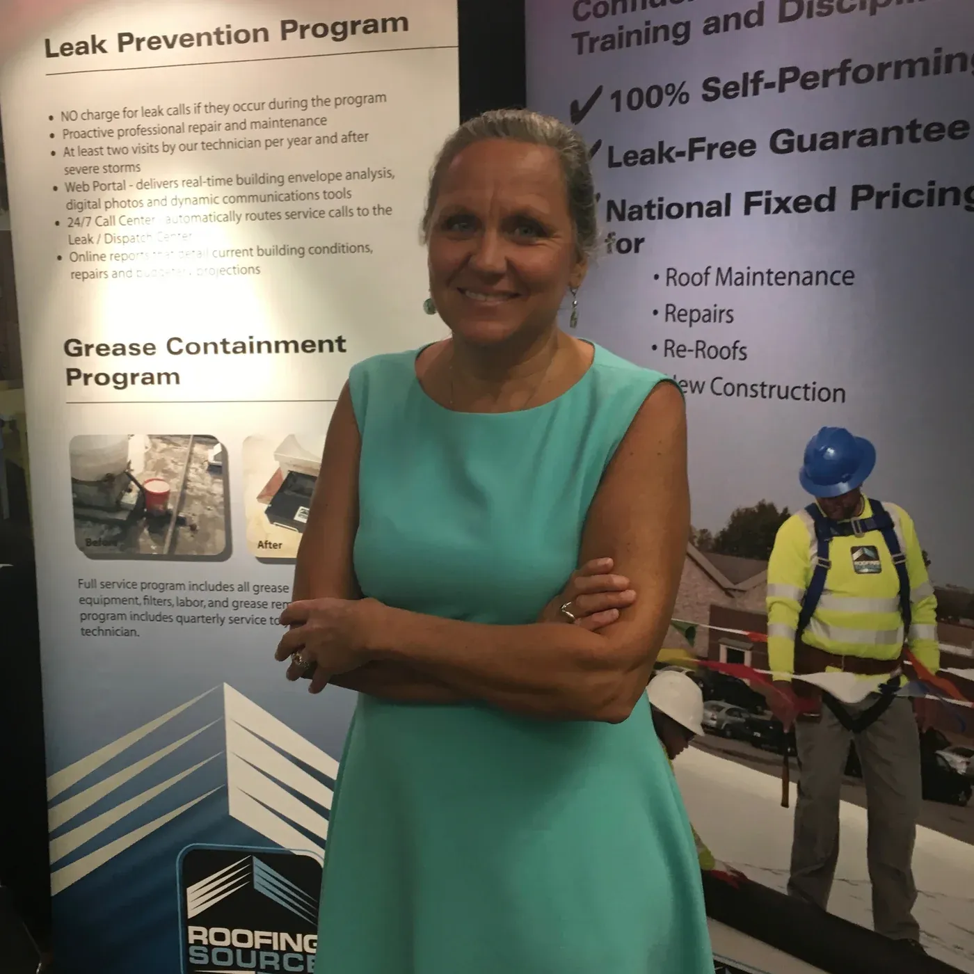 A woman in teal standing before two early RoofingSource trade-show banners.