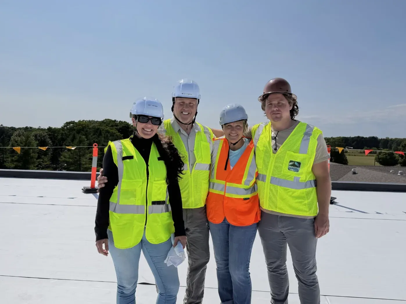 Four people in hi-vis vests and hard hats standing together on a white rooftop under a clear sky.