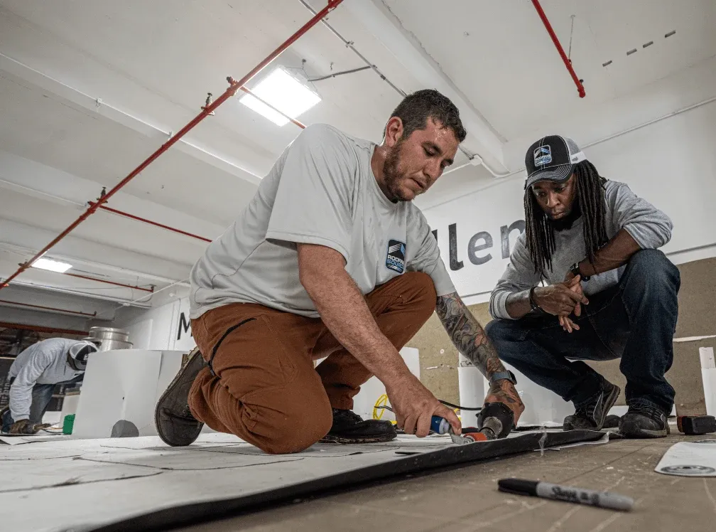 Two teammates seaming roofing membrane on the indoor mock roof decks in the training center.