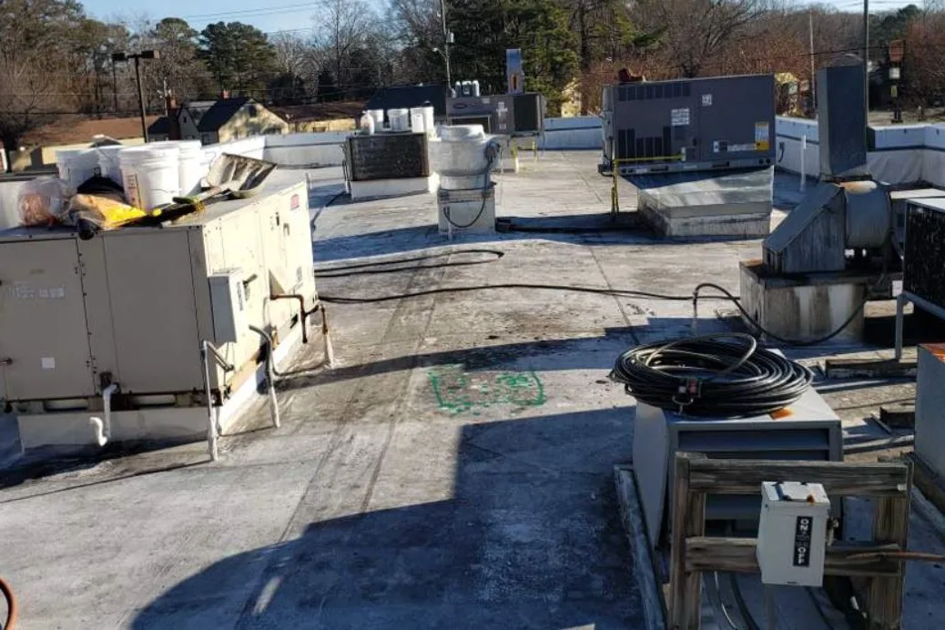 A grey, weathered commercial roof crowded with rooftop units before coating