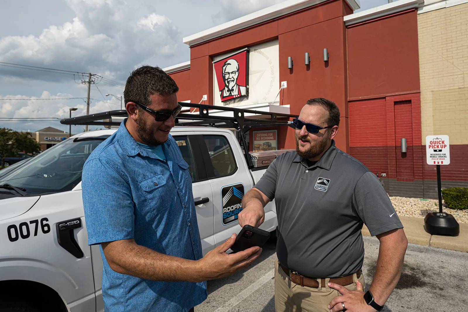 A RoofingSource teammate beside a company truck showing a phone screen to a restaurant operator