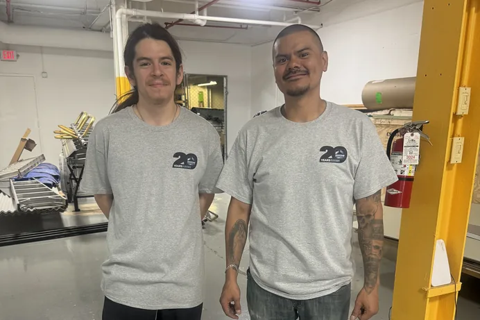 Two RoofingSource teammates in twenty-year company shirts standing on the shop floor