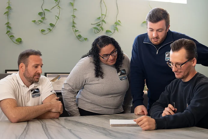 Four RoofingSource teammates working through a notebook together at headquarters