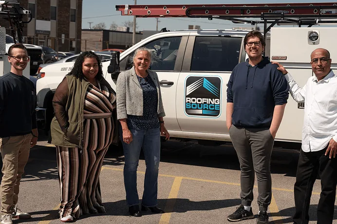 Five RoofingSource teammates standing together beside a company truck
