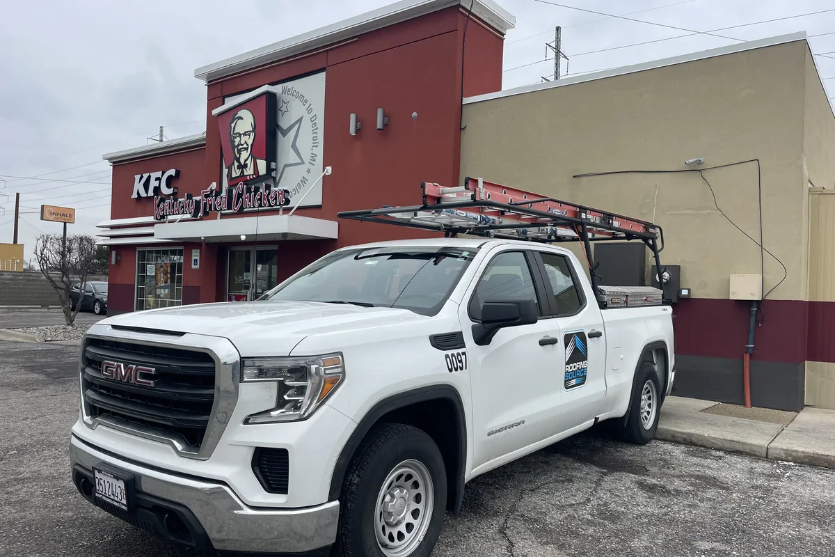 A RoofingSource pickup with a ladder rack parked outside a KFC restaurant