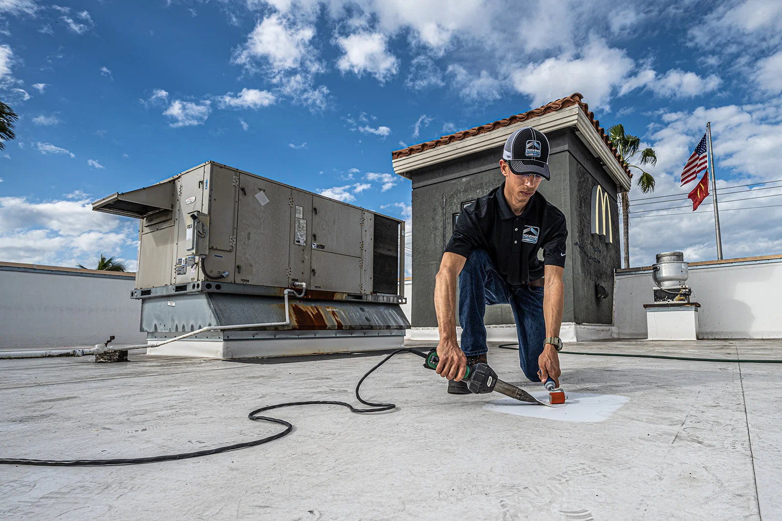 A Field Advisor kneeling on a white roof with a heat gun, sealing a repair