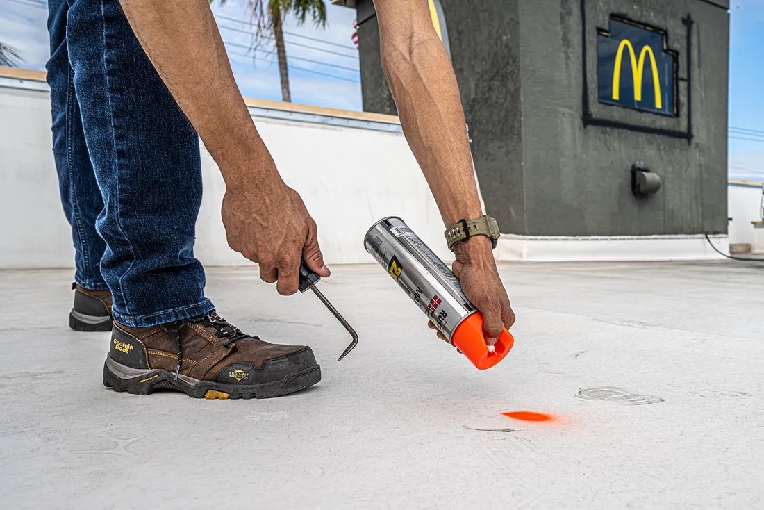 A teammate marking a defect on a coated commercial roof with spray paint