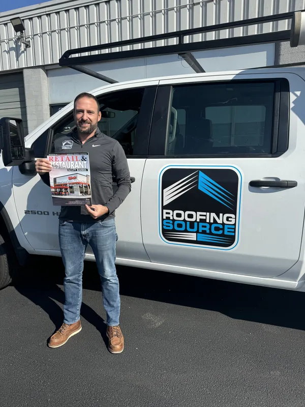 A teammate holding a trade magazine beside a company truck.