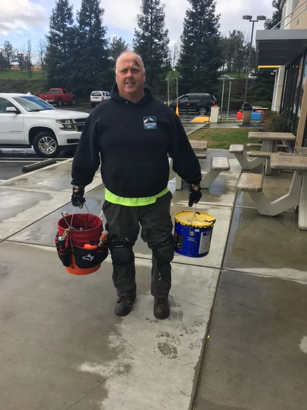 A teammate carrying two buckets across a restaurant lot.