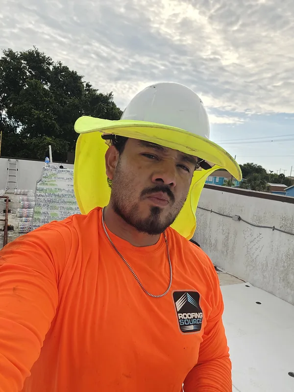 A Field Advisor in an orange shirt and a shaded hard hat, a selfie on a roof.