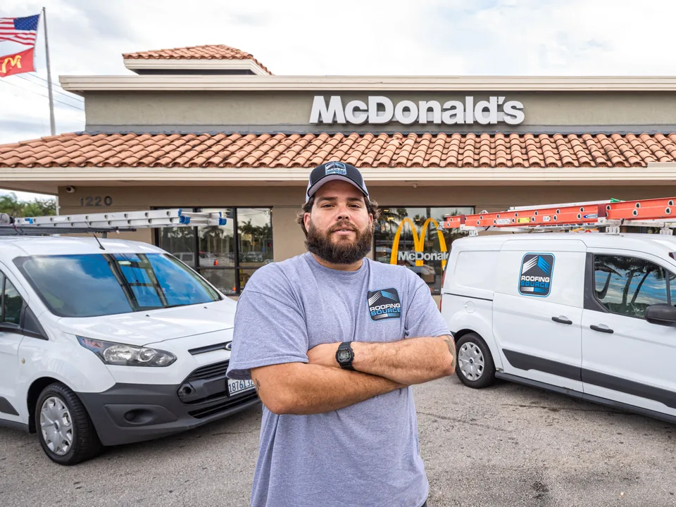 A teammate standing between two RoofingSource vans outside a restaurant.