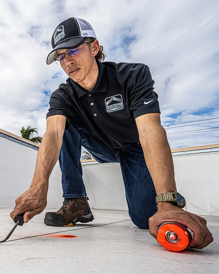 A RoofingSource Field Advisor kneeling at a parapet, sealing a seam on a commercial roof