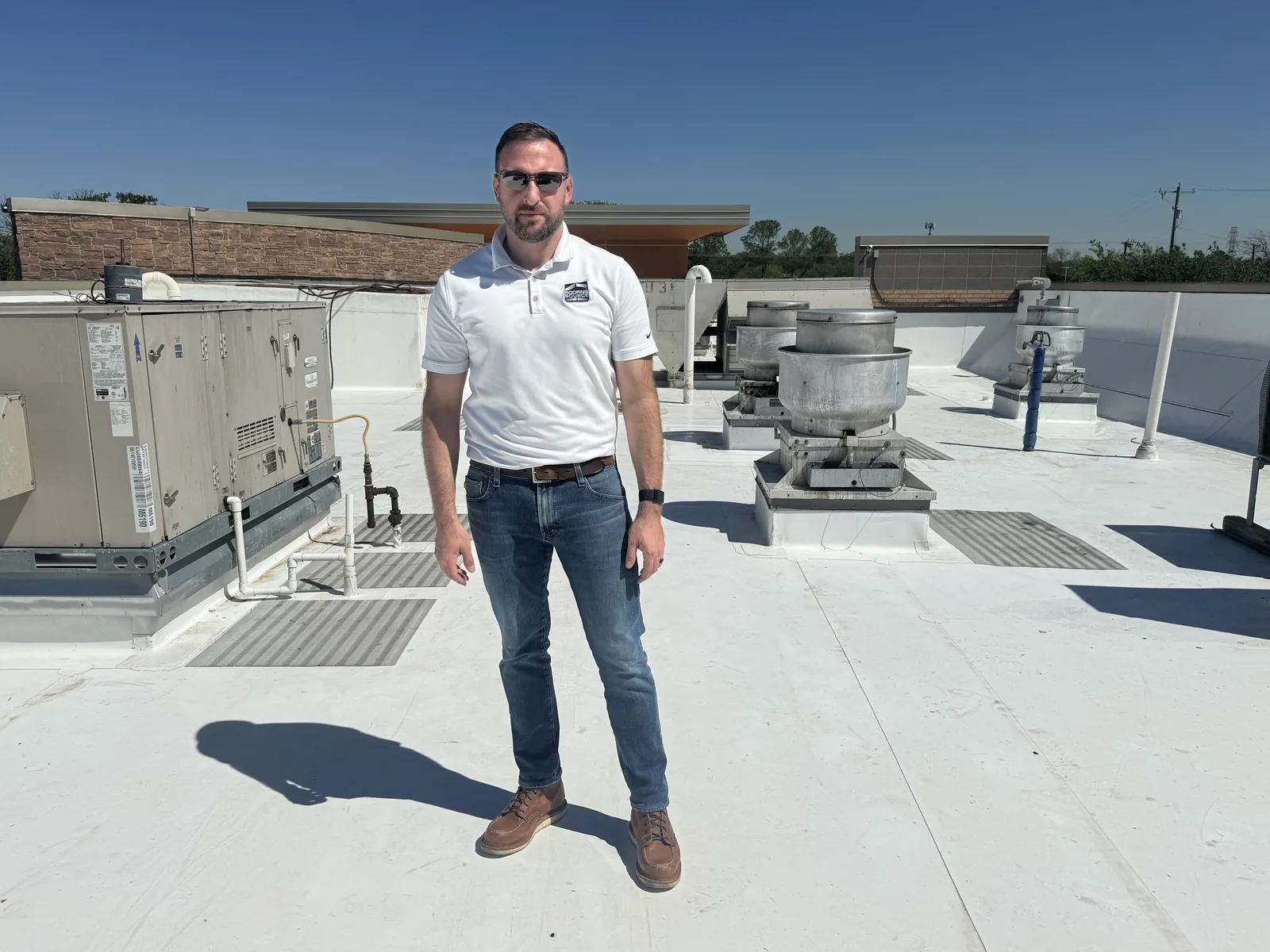 A Client Advisor in a white polo standing among rooftop units.