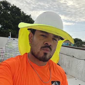 A Field Advisor in an orange shirt and a hard hat with a neck shade, on a commercial roof