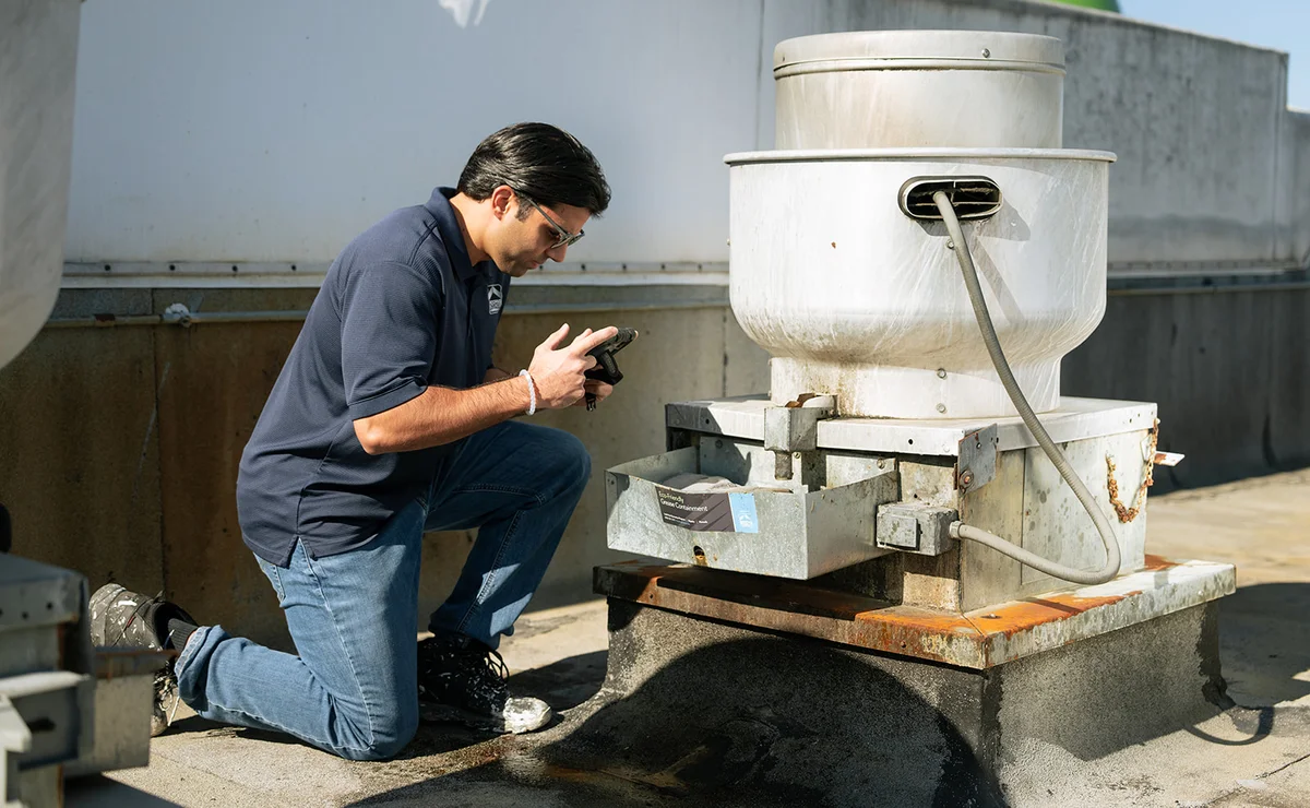 A teammate crouched beside a rooftop HVAC unit during a service visit