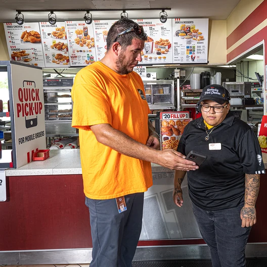 A Field Advisor talking with a restaurant manager at the counter inside a KFC