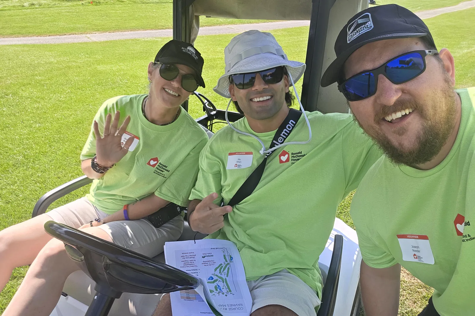 Three teammates in matching green shirts on a golf cart at a charity outing