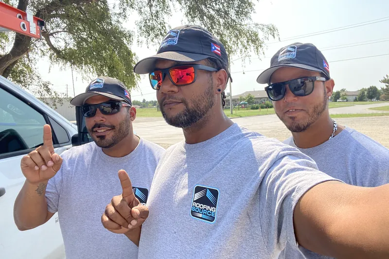 Three teammates in grey RoofingSource tees and caps, a selfie on a job site.