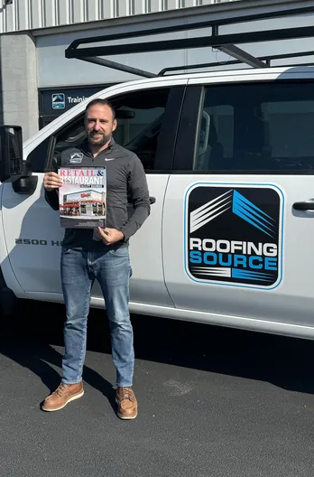 A RoofingSource teammate holding a trade magazine beside a company van