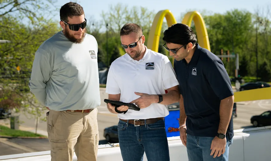 Three RoofingSource teammates reviewing a tablet on a rooftop