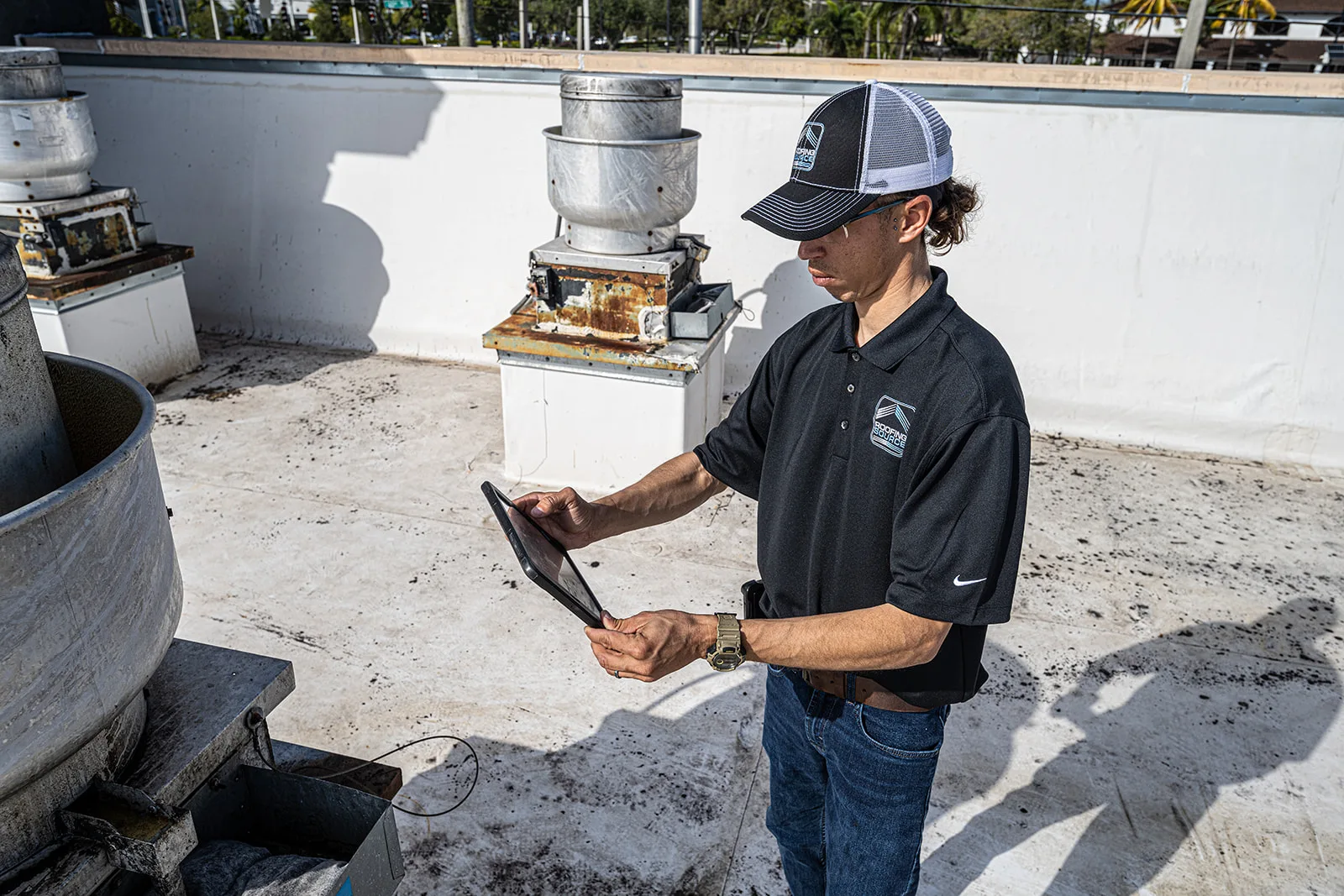 A RoofingSource teammate reading findings on a tablet beside a rooftop unit.