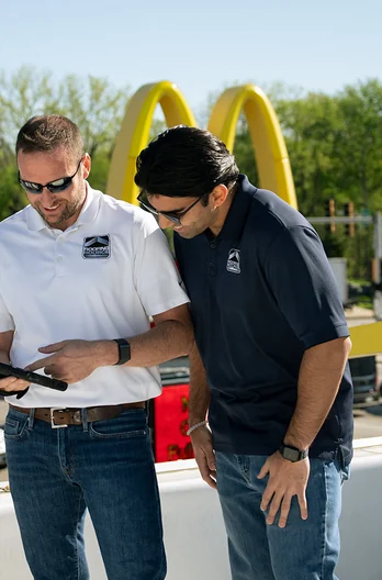 Two RoofingSource teammates reading a tablet together at a client site