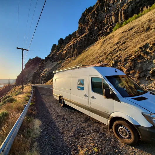 A RoofingSource van parked on a cliff road above a river at sunrise