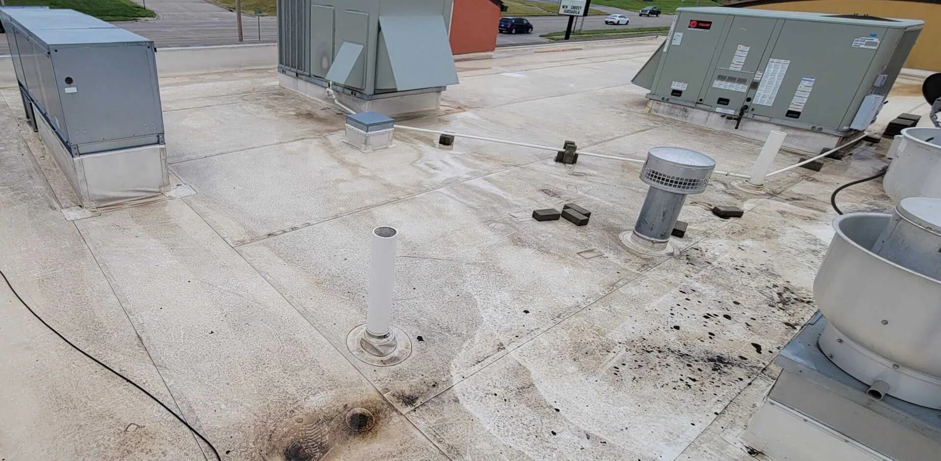 A stained commercial roof surface with a pipe boot and rooftop units before reroofing