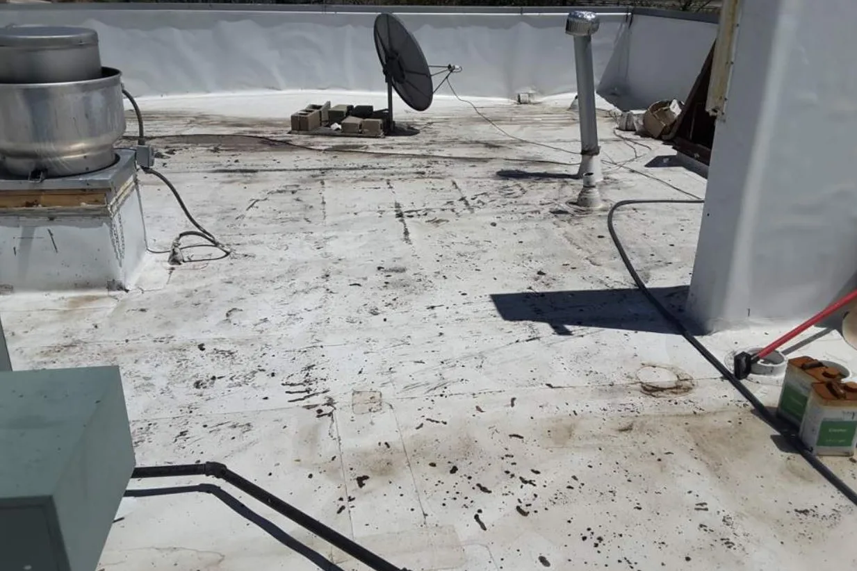 A corner of a commercial roof dark with debris around a satellite dish before restoration