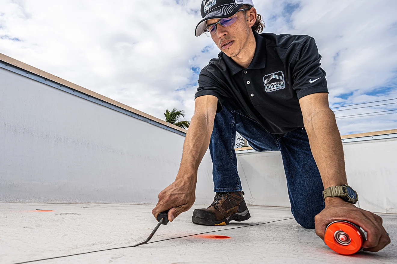 A RoofingSource Field Advisor kneeling on a white roof, testing a membrane seam with a probe
