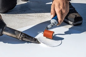A close-up of a teammate heat-welding a membrane patch, seam roller in hand