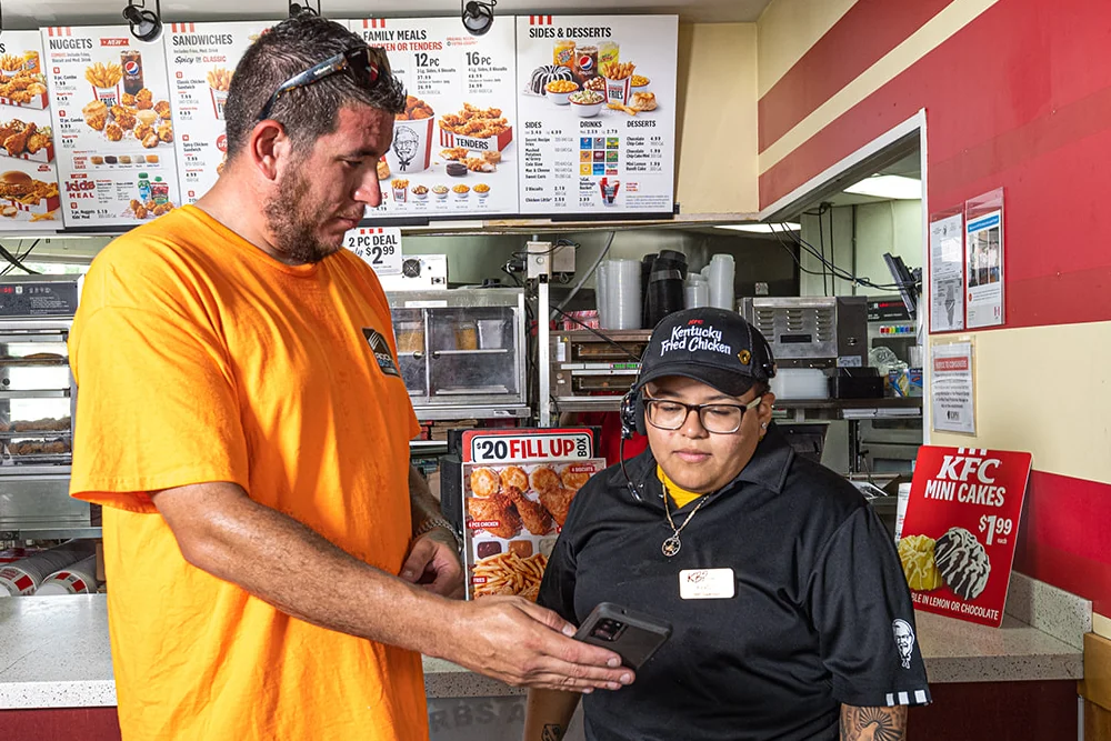 A RoofingSource teammate showing a report on a phone to a member of the client’s store team at the counter