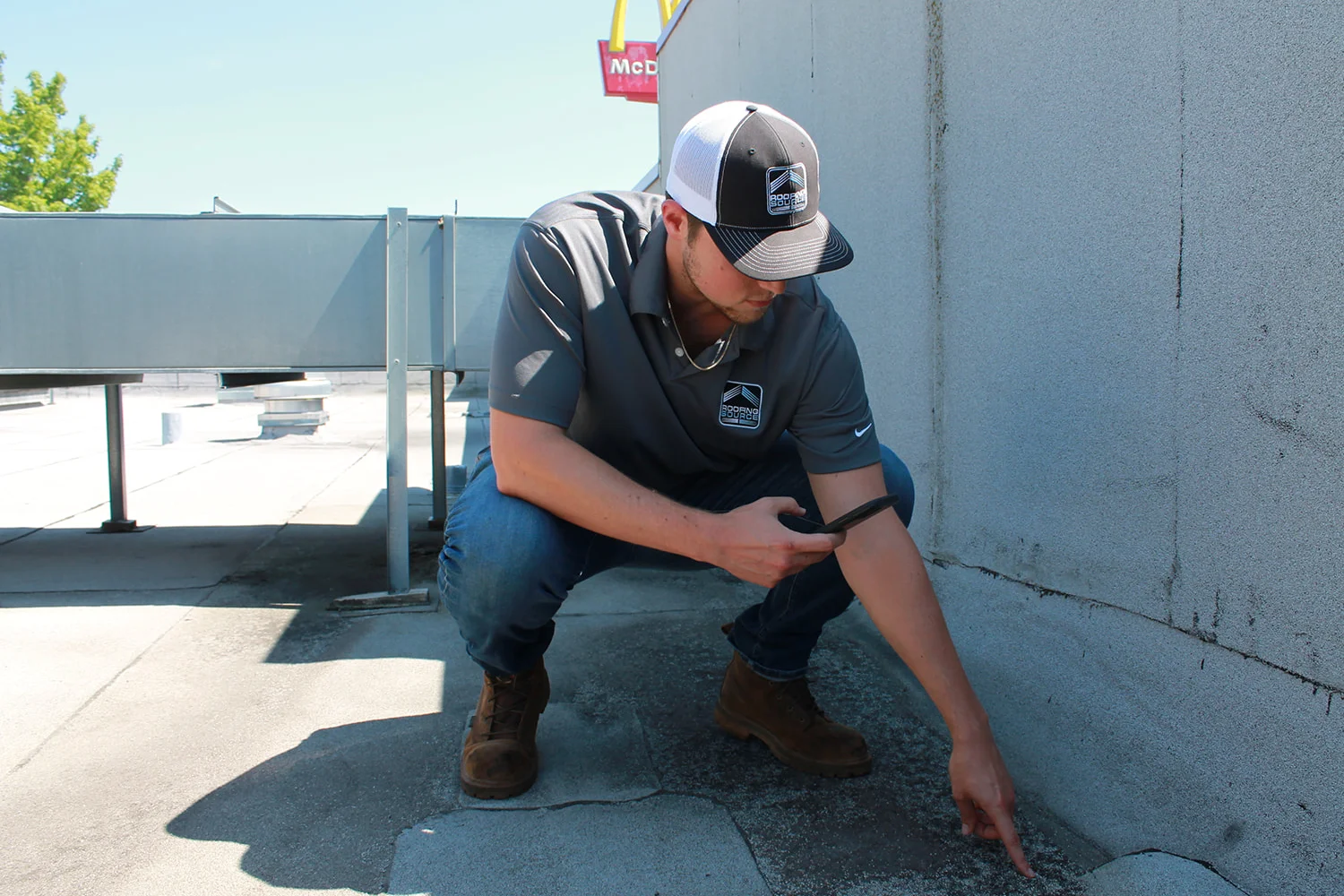A teammate crouched at a roof parapet, pointing out a defect